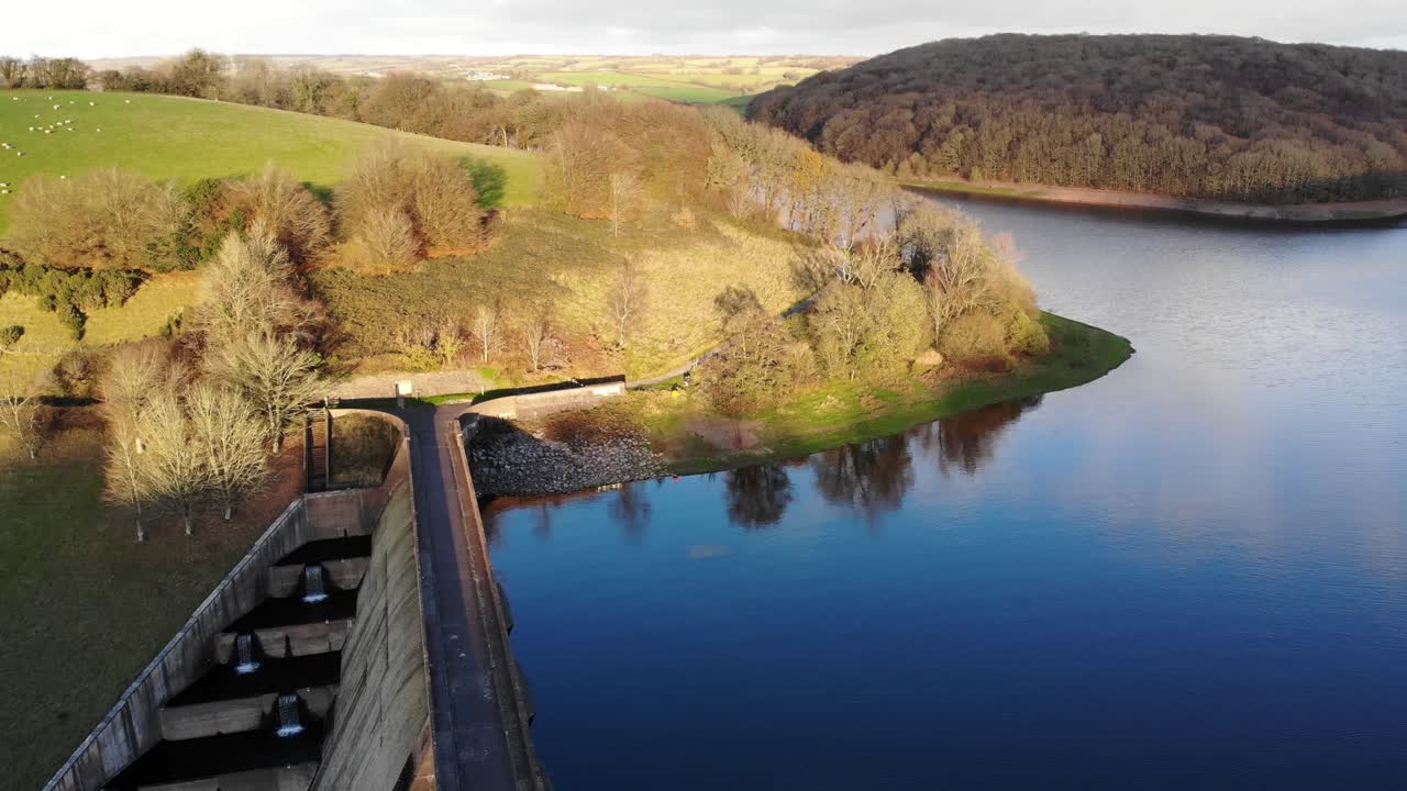 antena de una presa de hormigón de paredes altas en el lago wimbleball con colinas iluminadas por el sol en el fondo