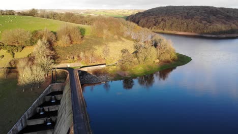 aerial of high walled concrete dam at wimbleball lake with sunlit hills in background