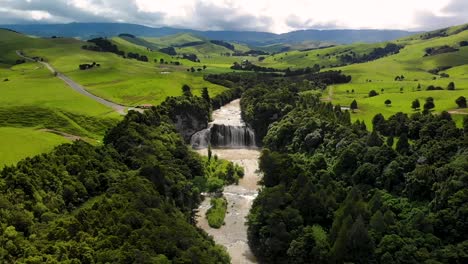 Beautiful-scenic-spot-with-waterfall,-surrounded-by-green-pastures,-New-Zealand,-Waihi-Falls---aerial-drone