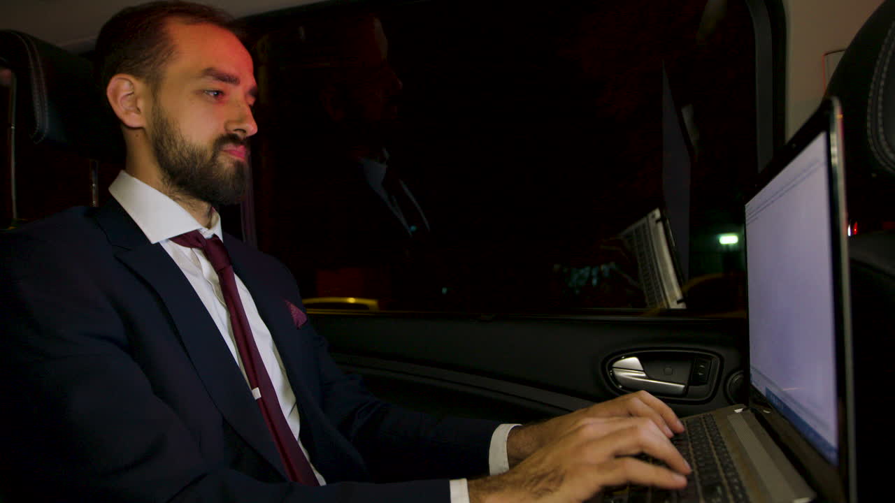 Uomo d'affari barbuto che digita sul laptop nel sedile posteriore della sua limousine