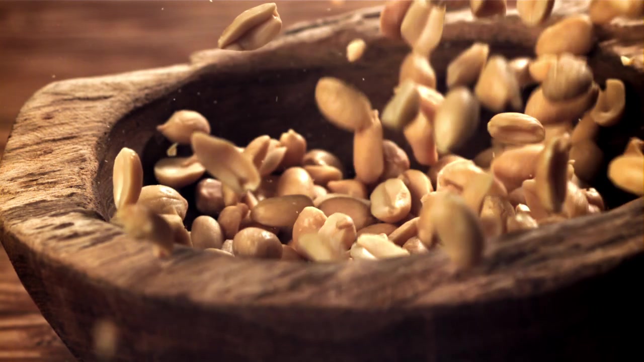 Slow Motion of Roasted Peanuts Falling into a Rustic Wooden Bowl