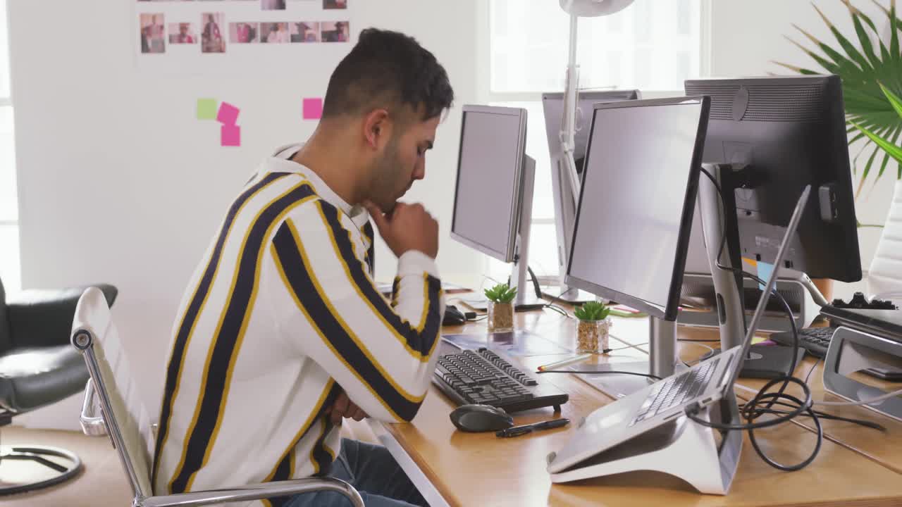 Mand af blandet etnicitet, der arbejder ved en computer på et kreativt kontor.