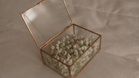 close up of wedding rings placed in a glass box with baby’s breath