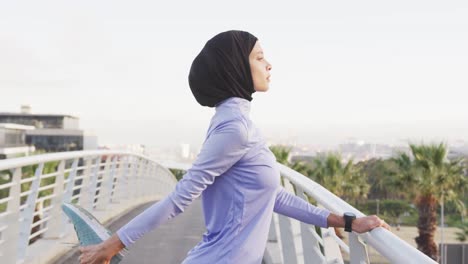 side view of woman wearing hijab stretching outside looking at camera