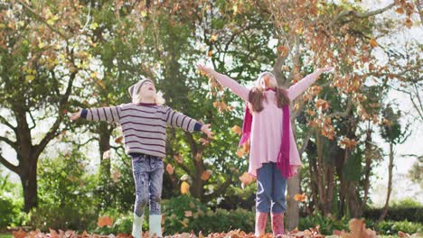 Video-of-happy-caucasian-brother-and-sister-having-fun-throwing-autumn-leaves-in-garden