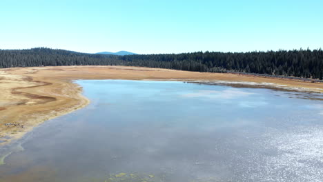 aerial flying left over dried up mountain lake with pine trees and hills