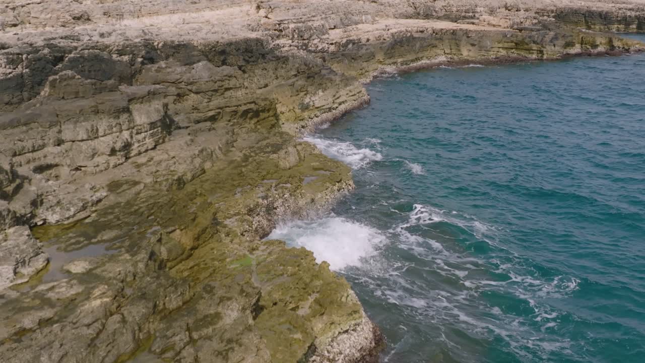 Slow motion aerial footage of waves hitting the rocks and shore in Polignano a Mare, Italy