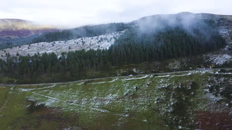 viaje a través de wicklow: seguimiento aéreo de un coche gris en medio de montañas brumosas y bosques cubiertos de nieve