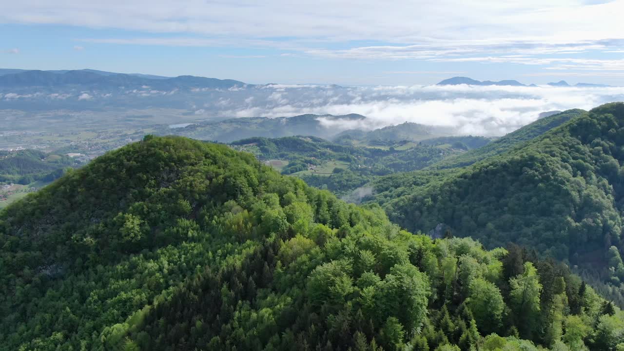 Green lush mountains and clouds in distant valley below, circle aerial