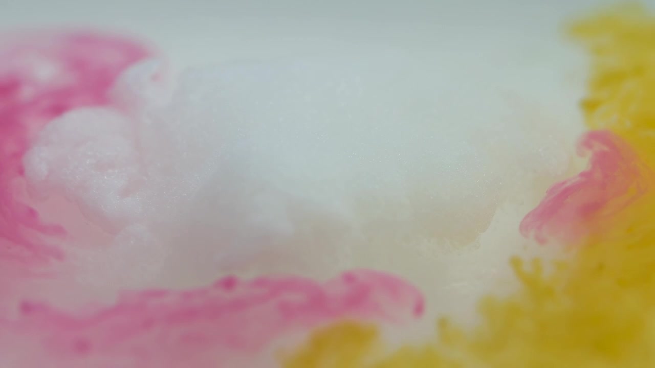 Pennacchi di colorante magenta e giallo che entrano e si diffondono in un serbatoio di vetro trasparente, ammorbidendo un pennacchio di crema bianca.