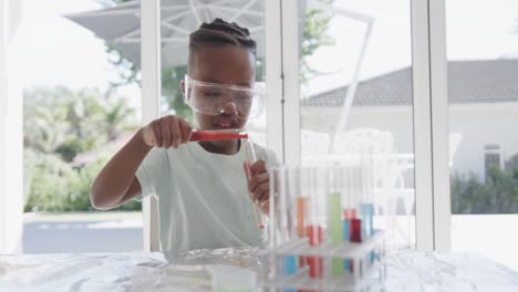 African-american-boy-sitting-at-table-holding-test-tubes-with-liquid,-in-slow-motion