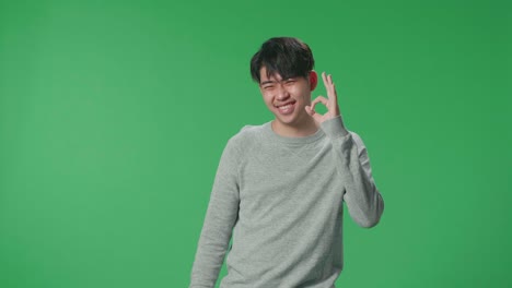 an happy asian man showing okay gesture to the camera in the green screen studio