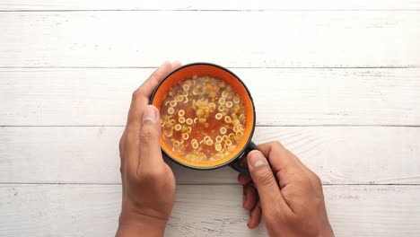 person holding a bowl of vegetable soup with noodles