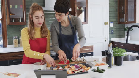 Feliz-Pareja-De-Lesbianas-Caucásicas-Preparando-Comida-Y-Usando-Una-Tableta-En-Una-Cocina-Soleada