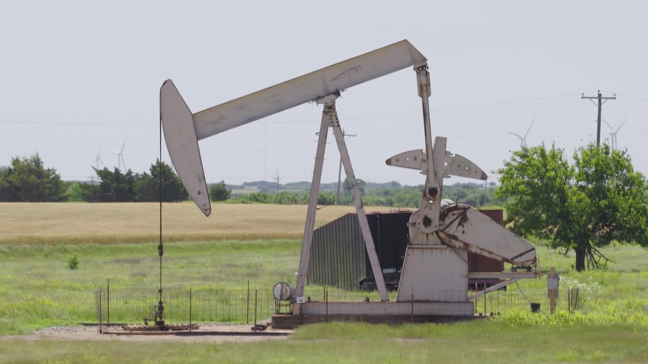 Drone 4K of a wheat field with two oil pump jacks and wind turbines in the background.