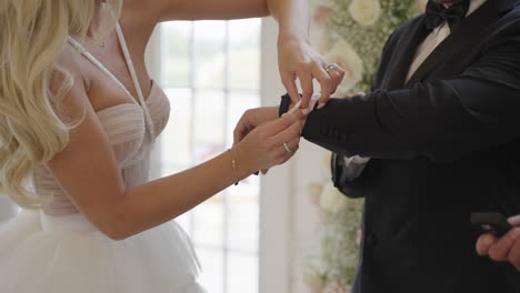 la novia ayudando al novio a usar gemelos para prepararse para la boda