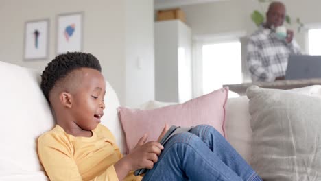 african american grandson using tablet with grandfather using laptop at home, slow motion