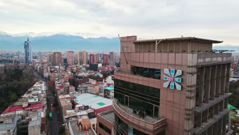 órbita-Aérea-De-Un-Reloj-En-La-Parte-Superior-Del-Edificio-De-Comercio-En-El-Centro-De-Santiago-Con-Edificios-Residenciales-Al-Fondo,-Chile