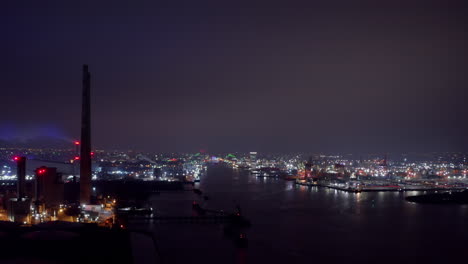 Drone-ascends-above-Poolbeg-with-entrance-of-Dublin-Harbor-at-night,-iconic-powerstacks