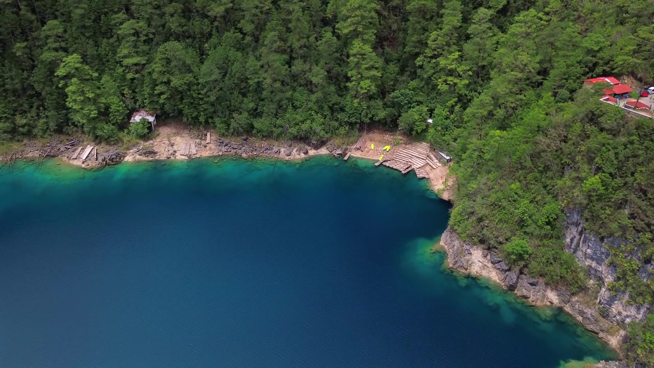 Ripresa aerea ad alto angolo di una laguna blu profondo circondata da una rigogliosa foresta di pini verdi e moli in legno a Lagunas de Montebello, Chiapas, Messico