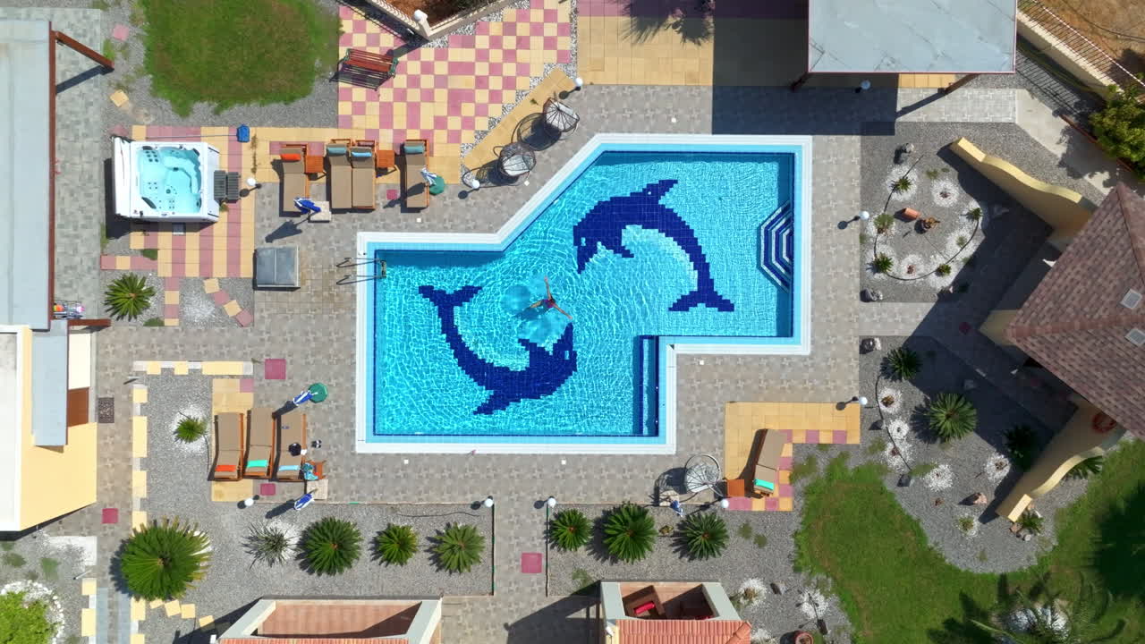 Birds eye drone shot above a woman swimming in a pool at a resort in sunny Greece