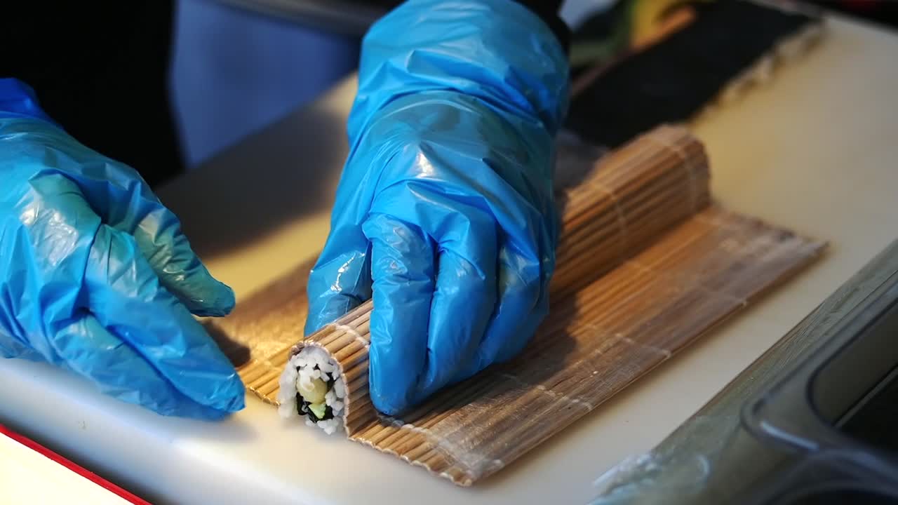 Chef professionista che prepara rotoli di sushi con guanti blu