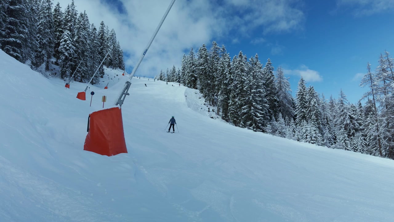 Sciatore che scende un pendio innevato oltre alberi invernali e segnaletica di sicurezza. Scattato con uno smartphone.