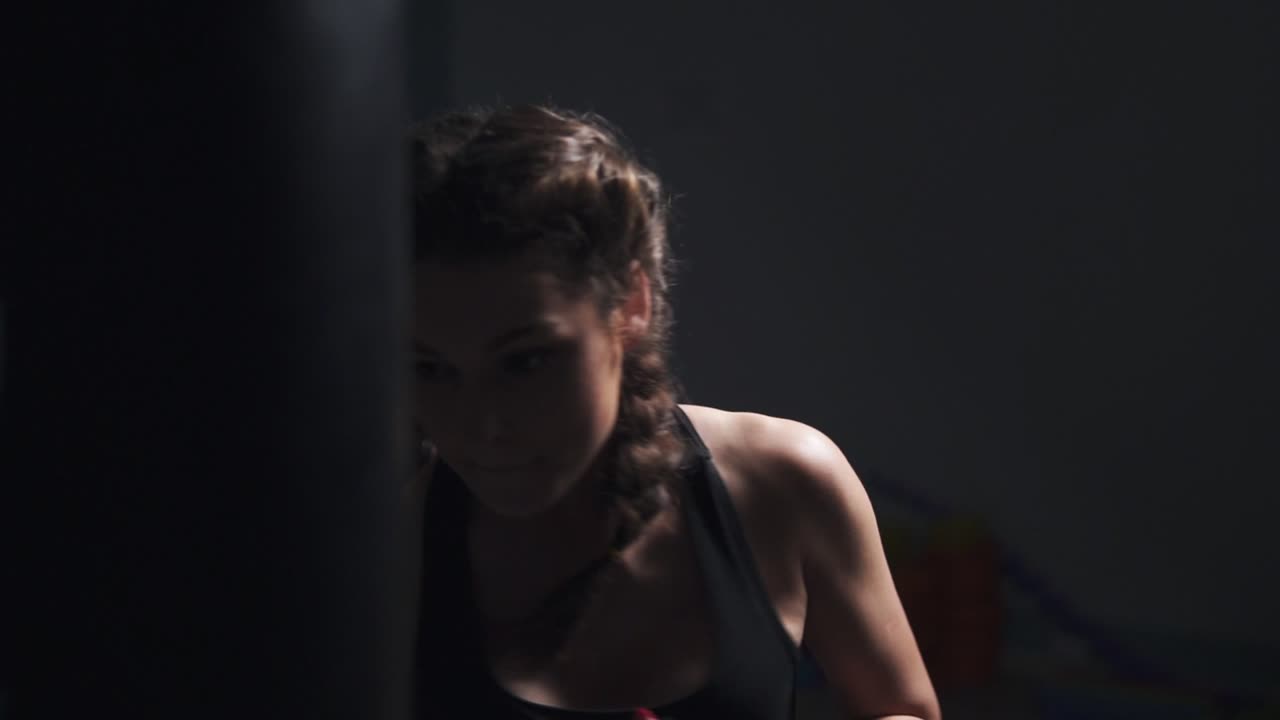 Young woman in boxing gloves training with a punching bag in a boxing club. Slow Motion shot