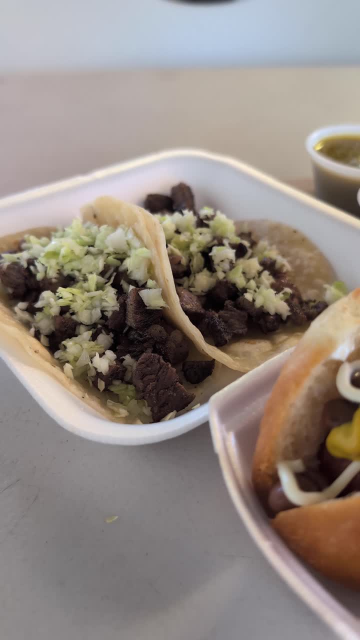 En lodret video, der starter med en carne asada taco og panorerer til højre til en Sonoran hotdog med bønner, saucer og toppings. Glatte bevægelser fremhæver klassiske teksturer fra Southwest street food