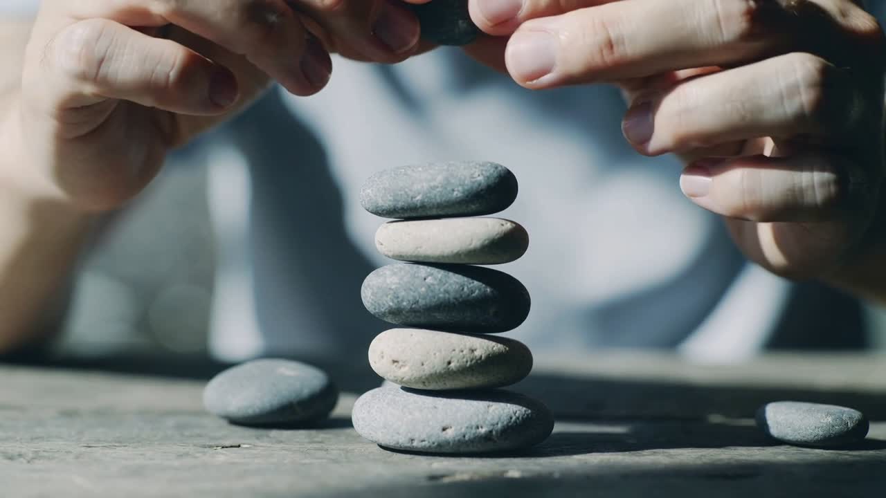 Hombre sosteniendo una piedra adicional sobre una columna, bajando y ajustando piedras en un tablero de madera para equilibrar.