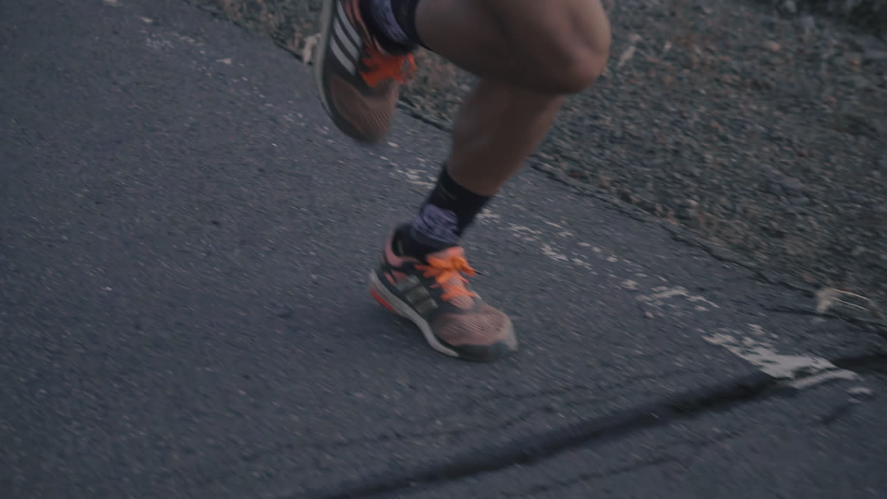 Close up shot of professional runners feet and legs running on paved road in slow motion at dusk shot in HD