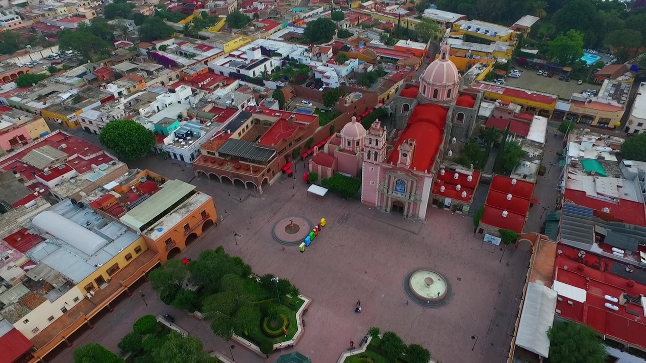 Vista aerea con drone di un grande complesso ecclesiastico con cupole e edifici coloniali circostanti attorno a una piazza aperta, tetti colorati e layout urbano che mostrano architettura culturale e vita cittadina.
