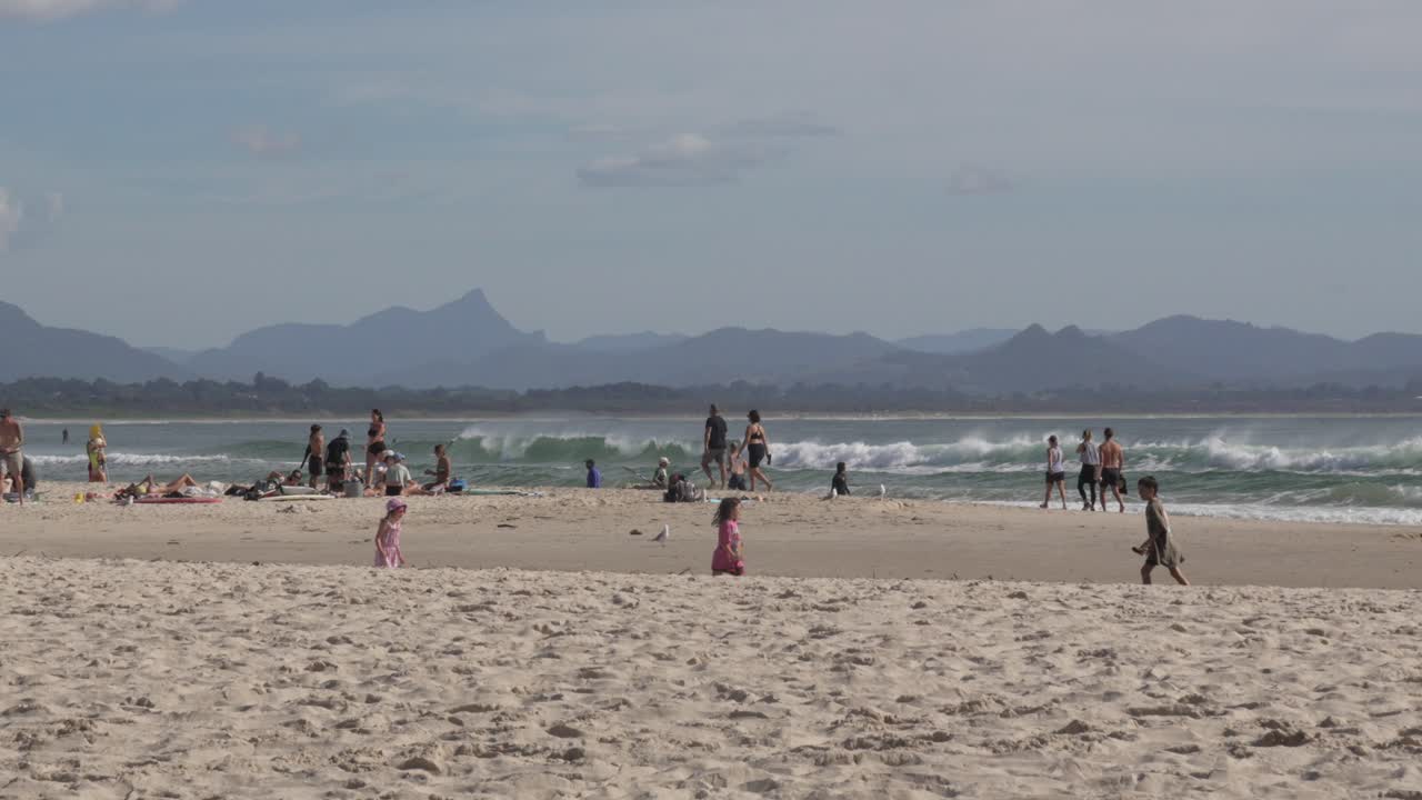 Sandy beach shore ocean sea waves, people group walking Australia Byron Bay