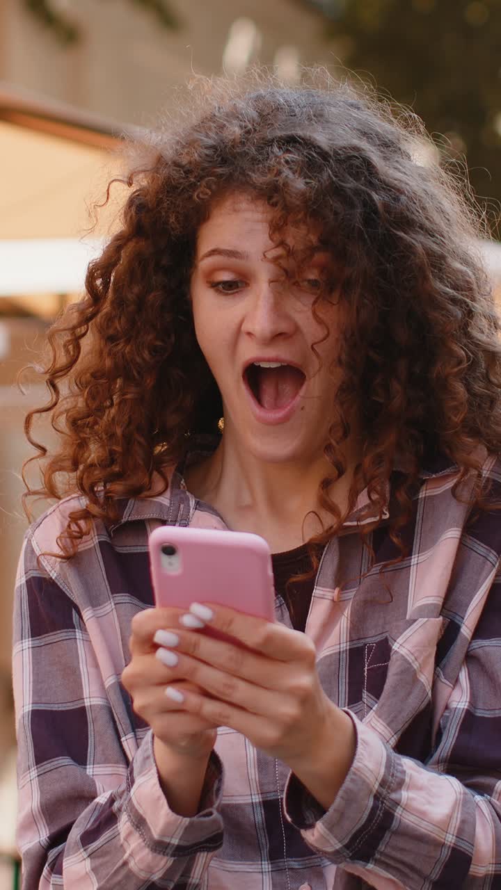 emocionada feliz ganadora mujer joven usa teléfono inteligente celebrando ganar buenas noticias de mensaje en la calle de la ciudad