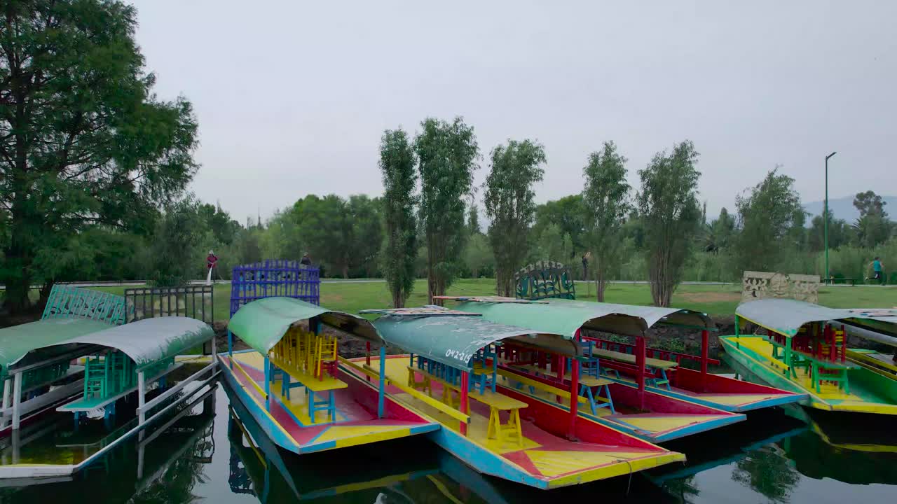Pull- left to right above a lake, with view of mexican boats named trajineras in Xochimilco, Mexico City