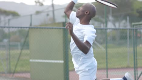 Afroamerikanischer-Männlicher-Tennisspieler,-Der-In-Zeitlupe-Den-Ball-Auf-Dem-Tennisplatz-Im-Freien-Serviert