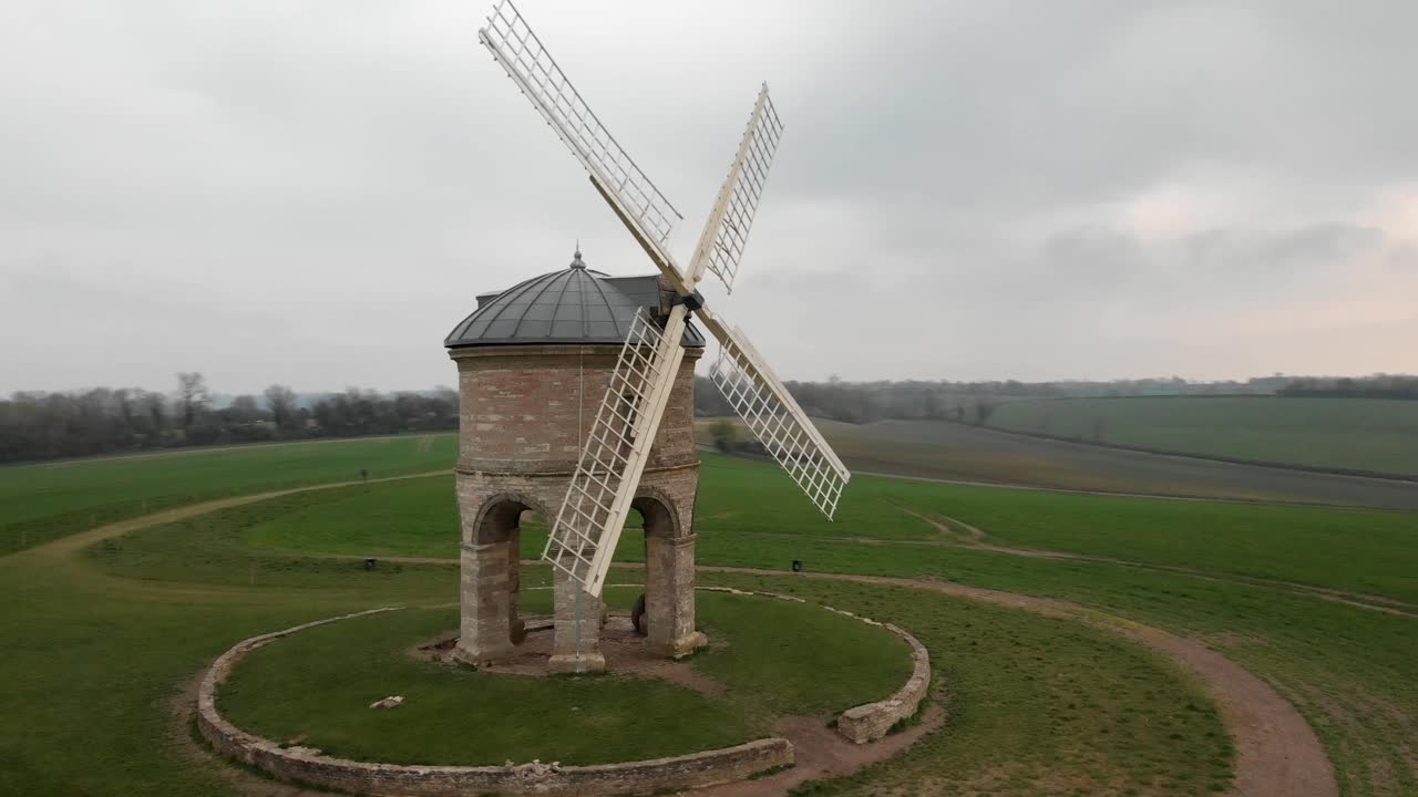 Spinning aerial shot showcasing a historic windmill surrounded by lush fields.