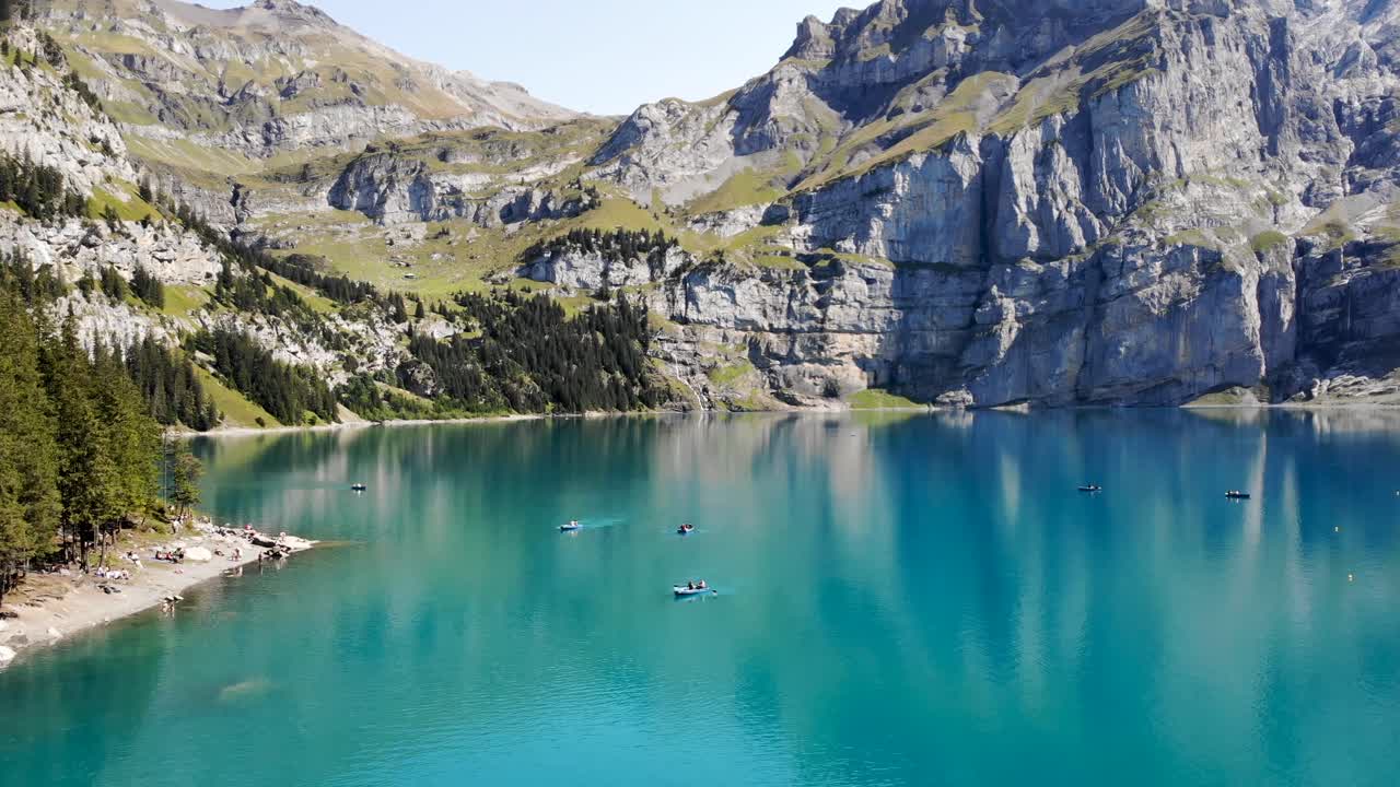 sobrevuelo aéreo sobre el agua turquesa del lago oeschinensee en kandersteg, suiza, con vistas a barcos y acantilados en una soleada tarde de verano