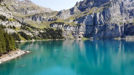 aerial flyover over the turquoise water of lake oeschinensee in kandersteg, switzerland with views of boats and cliffs on a sunny summer afternoon