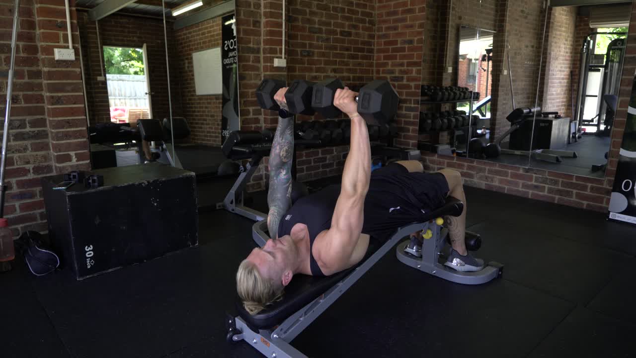 홈 체육관에서 문신을 한 남자 감소 아령 벤치 프레스 무거운 무게