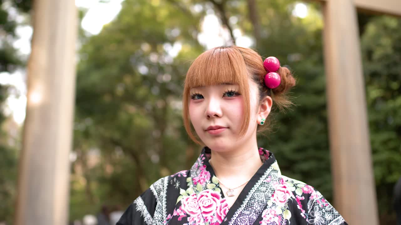 Una donna che indossa una yukata floreale si trova davanti a un cancello torii in un parco boscoso