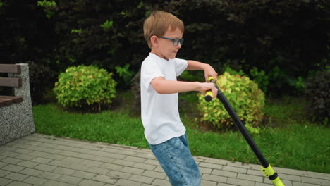 a young boy spins his scooter energetically in an anti-clockwise direction on an interlocked path in a park