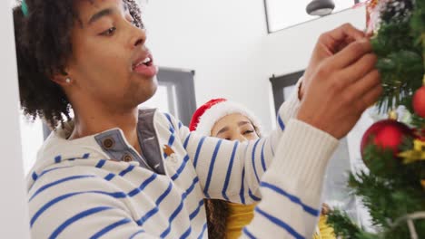 Video-De-Una-Feliz-Pareja-Diversa-Con-Cuernos-De-Reno-Y-Gorro-De-Papá-Noel-Decorando-El-árbol-De-Navidad-En-Casa