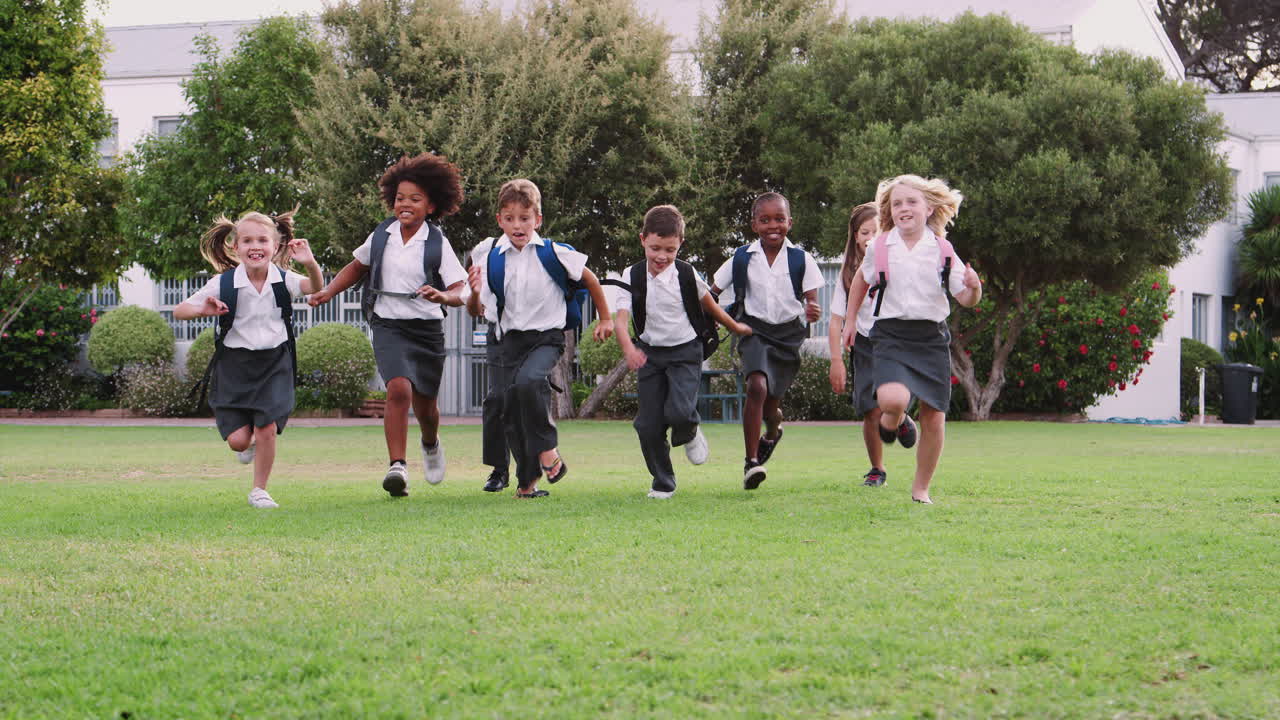 Excited Elementary School Pupils Wearing Uniform Running Across Field At Break Time
