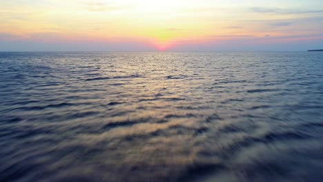 low flying drone dolly above ocean water to setting sun over the horizon, motion blur