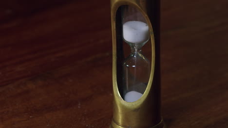 time passes, granules sift through brass hour glass timer on wood desk