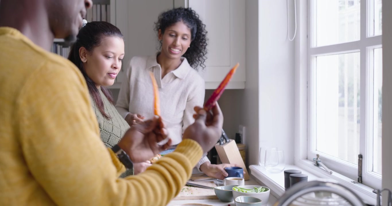 African American man rinsing colander in sink after hands comparing carrots, friends prepping meal