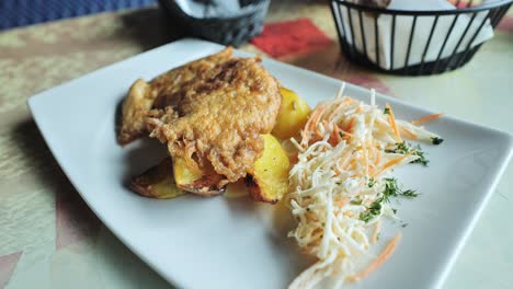 crispy chicken, potatoes on a white plate - complemented with coleslaw and herbs