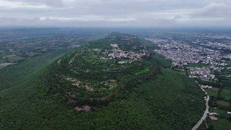 vast walled fortress with small town on lush green mountain top, rajasthan, india. drone aerial. reveal.