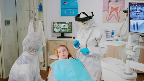 pediatric dentist in protective shield checking teeth of little girl